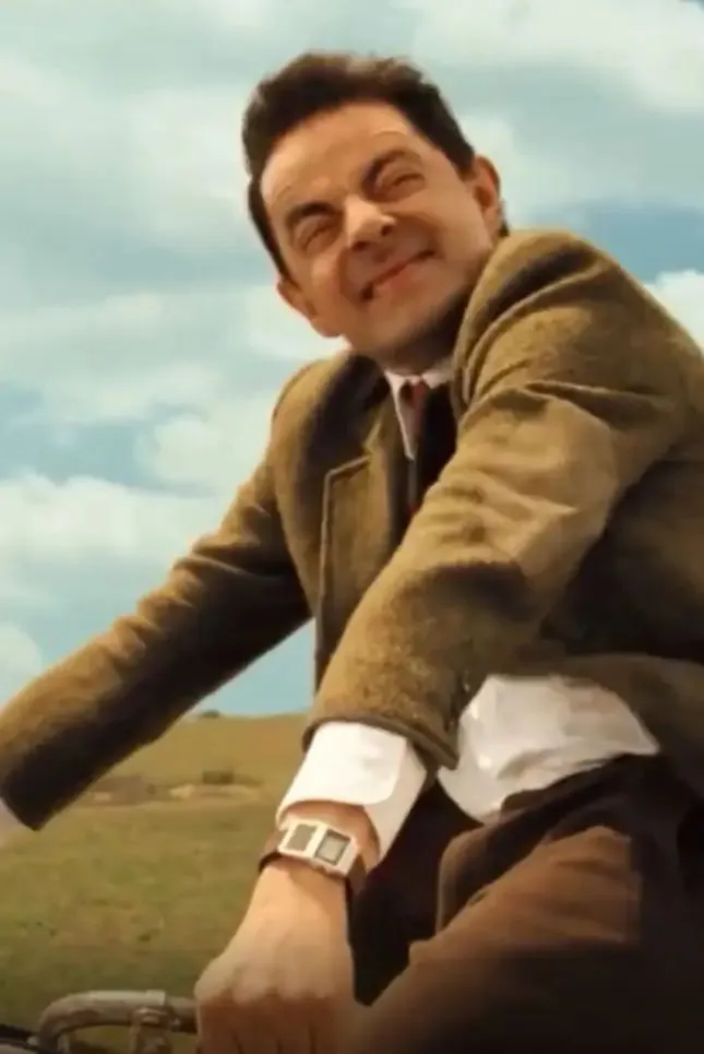 Mr. Bean rides a vintage bicycle with a front basket filled with produce.